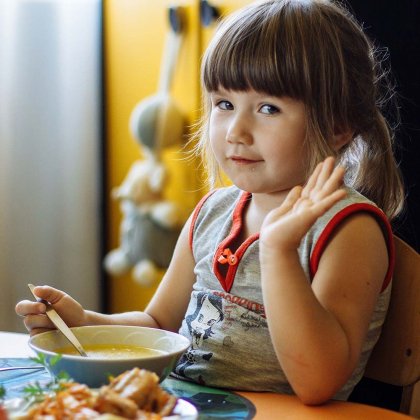 Kind mit einer warmen Suppe winkt in die Kamera
