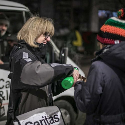 Caritas Mitarbeiterin teilt im Freien Suppe an einen Menschen aus